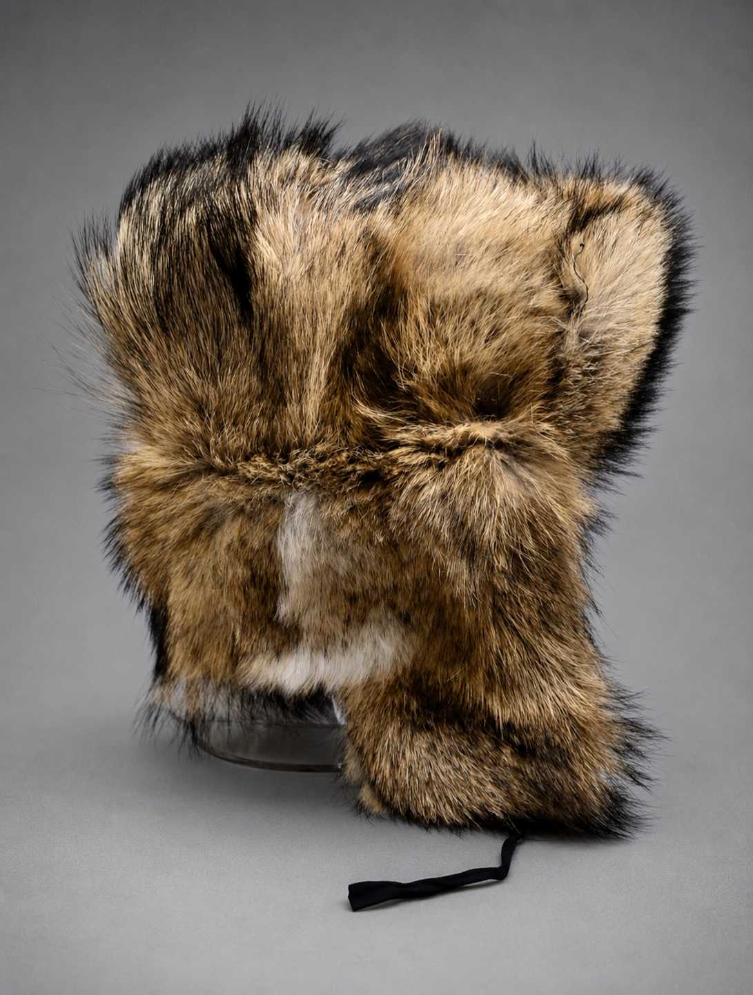 Handcrafted coyote fur ushanka hat made from premium natural coyote fur with ear flaps, photographed in a professional gray studio setting.